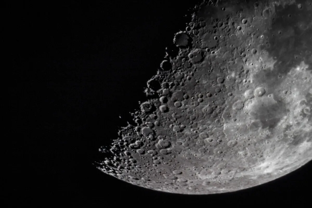 A close view of a crescent Moon with visible crater shadows near the terminator, as seen through binoculars