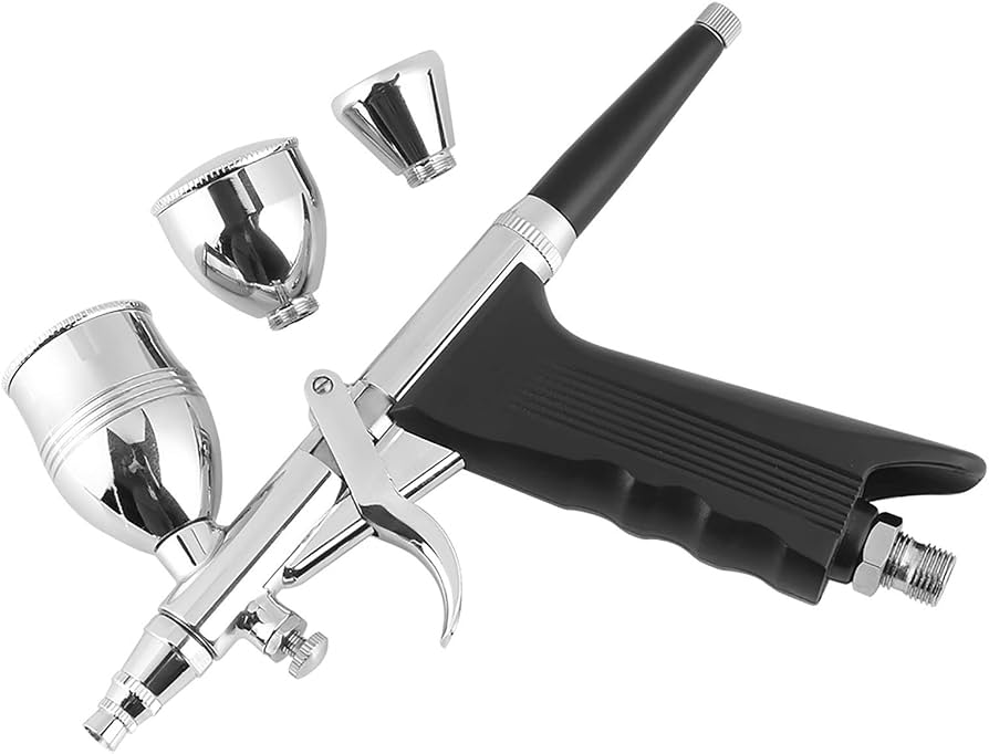 A hobbyist using a dual-action airbrush to spray primer onto model kit parts held on clips, with a small compressor on the floor beside the workbench