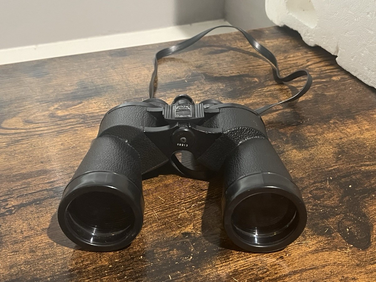 A pair of black 10x50 binoculars resting on a wooden table near a notebook and a small red flashlight