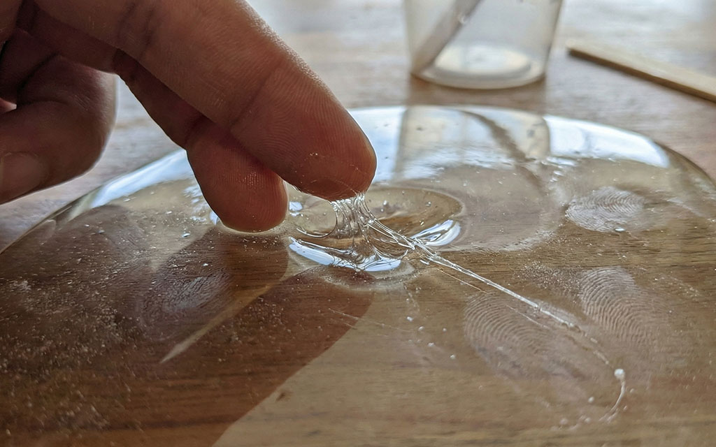 A photograph of a gloved hand touching a cured resin tray that has a visibly tacky, fingerprint-marked surface