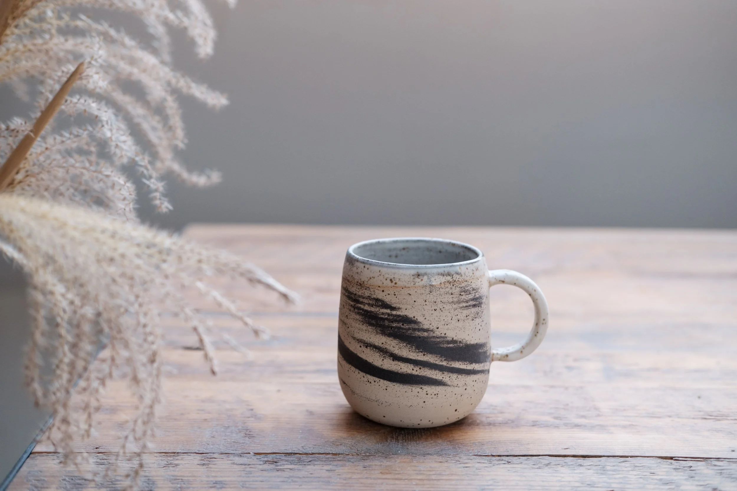 A plain ceramic mug on a table near a window casting a soft shadow, ready for a beginner still life drawing