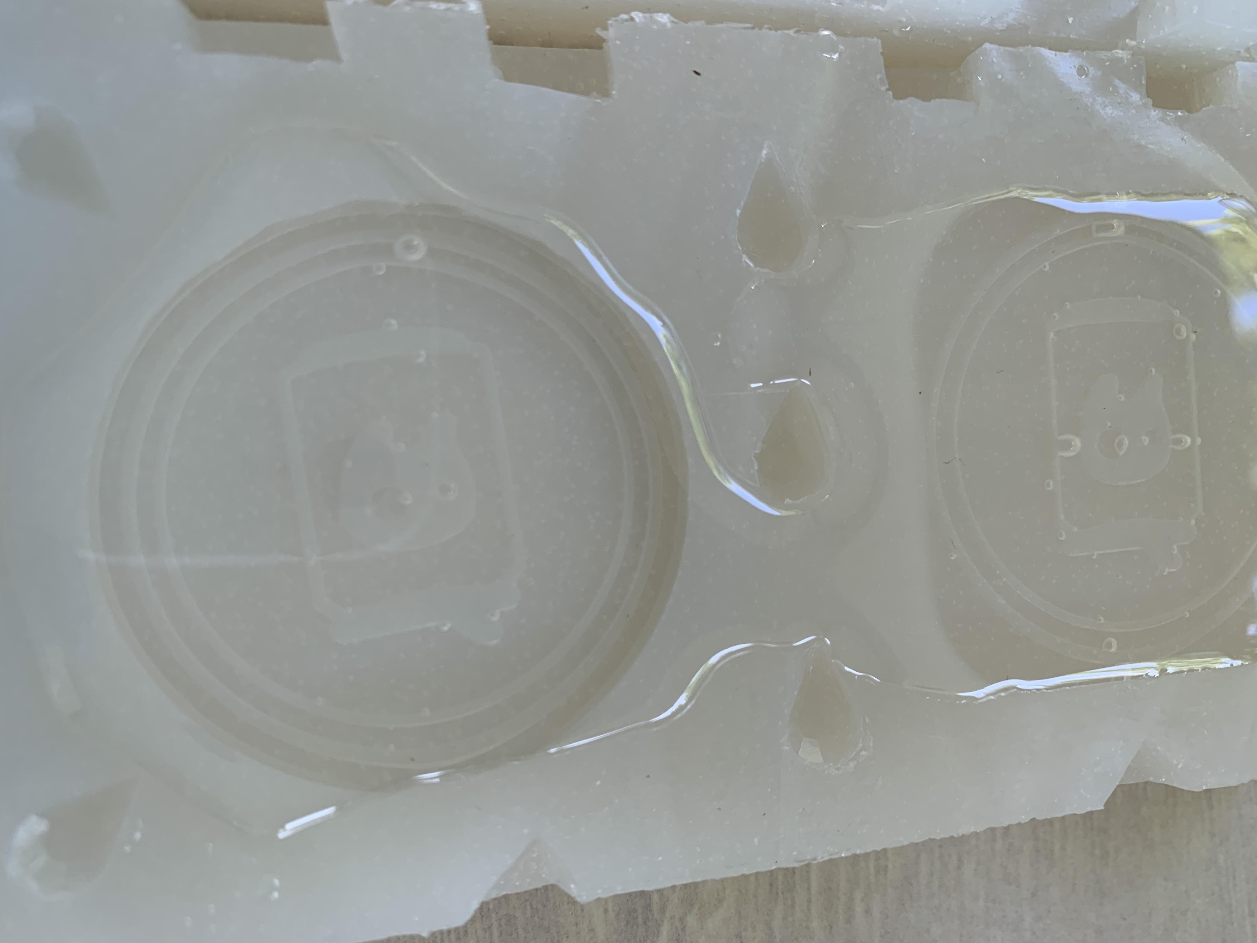 A tabletop photo of silicone resin molds partially filled with clear resin, showing tiny bubbles clinging to the sides and corners of the mold cavities