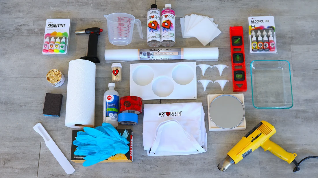 A tidy craft table set up for resin work with nitrile gloves, measuring cups, wooden stir sticks, a small digital scale, and a resin kit arranged neatly