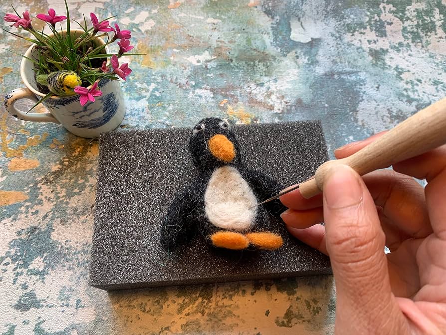 Hands needle felting a small wool shape on a rectangular foam mat that protects the tabletop