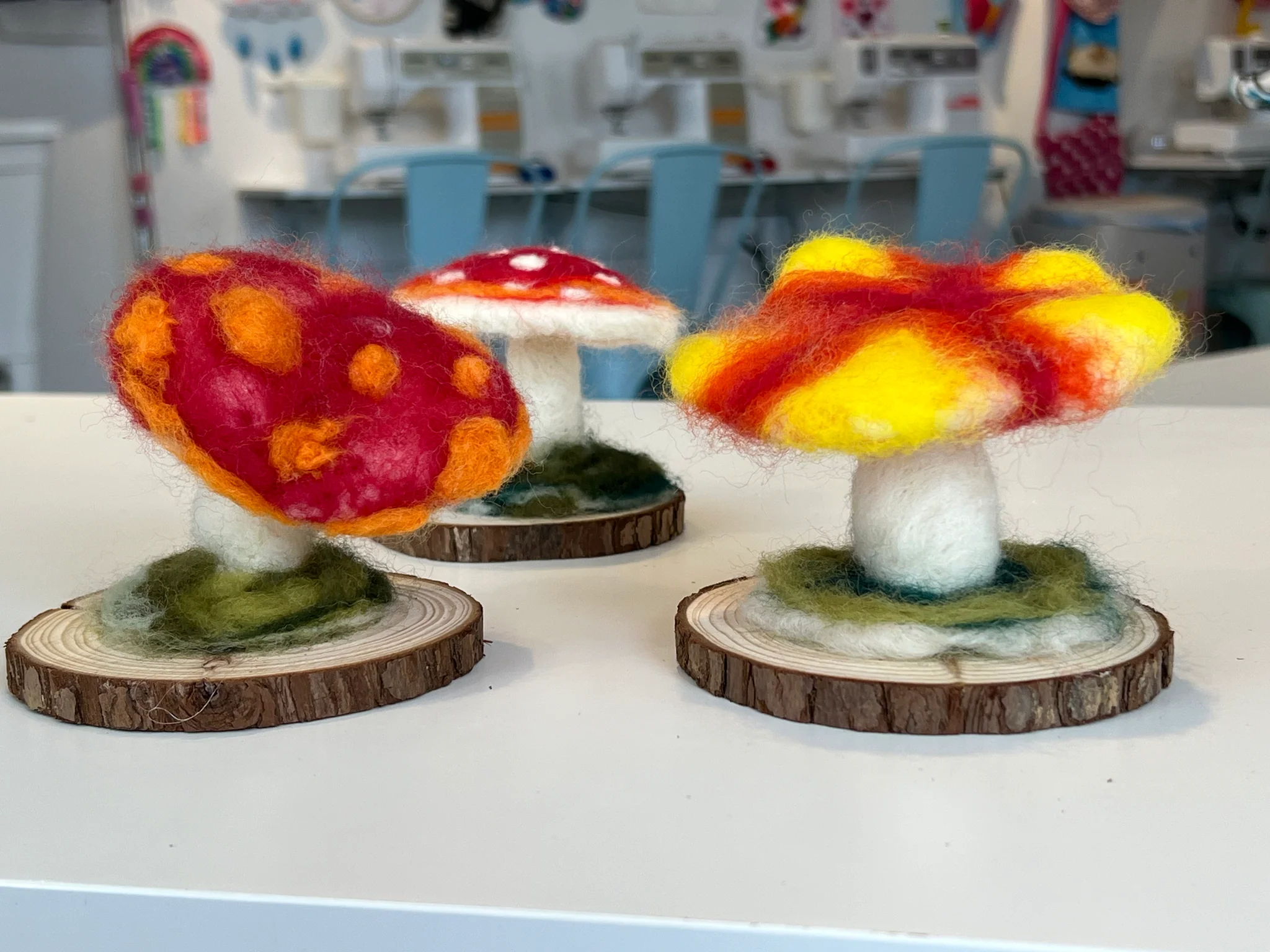 Small handmade needle felted mushroom with a red cap and pale stem sitting on a crafting table near loose wool fibers